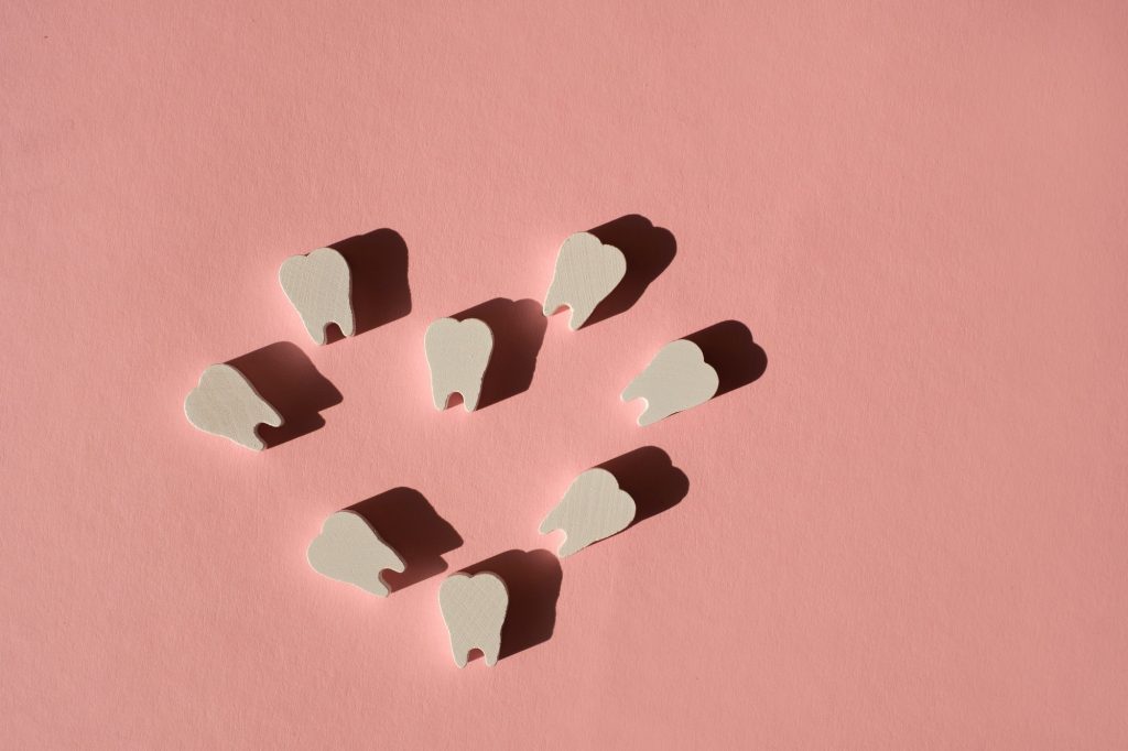 White models of teeth are laid out in the shape of a heart on a pink background.