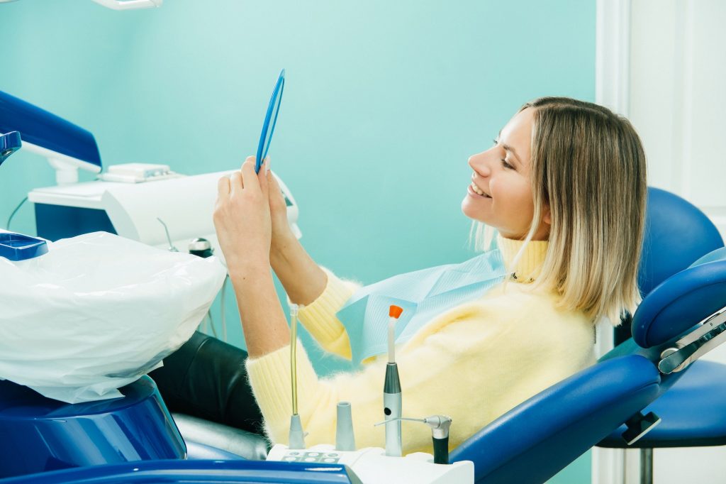 The girl smiles and looks in the mirror in dentistry